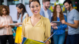 Portrait of smiling female executive holding clipboard and file in office